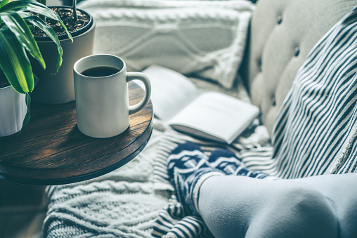 A young woman who is enjoying a cup of coffee while relaxing on a sofa. Conveys warmth and comfort in a relaxing environment.