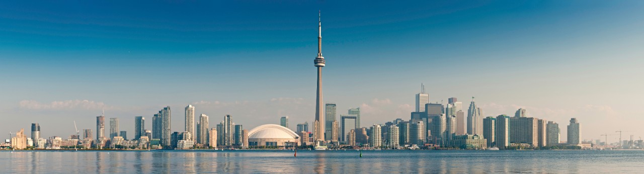 Clear blue panoramic skies over the landmarks of Toronto, the iconic spire of the CN Tower, white stadium dome of the Rogers Centre, the luxury harbour-side condominiums and the skyscrapers of the downtown business district reflecting in the still blue waters of Lake Ontario, Canada. ProPhoto RGB profile for maximum color fidelity and gamut.